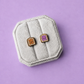 Peanut butter and jelly shaped enamel stud earrings in a white jewelry box on a light purple background
