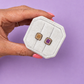 Hand holding a white jewelry box with Peanut butter and jelly shaped enamel stud earrings on a light purple background
