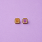 Peanut butter and jelly shaped enamel stud earrings on a light purple background