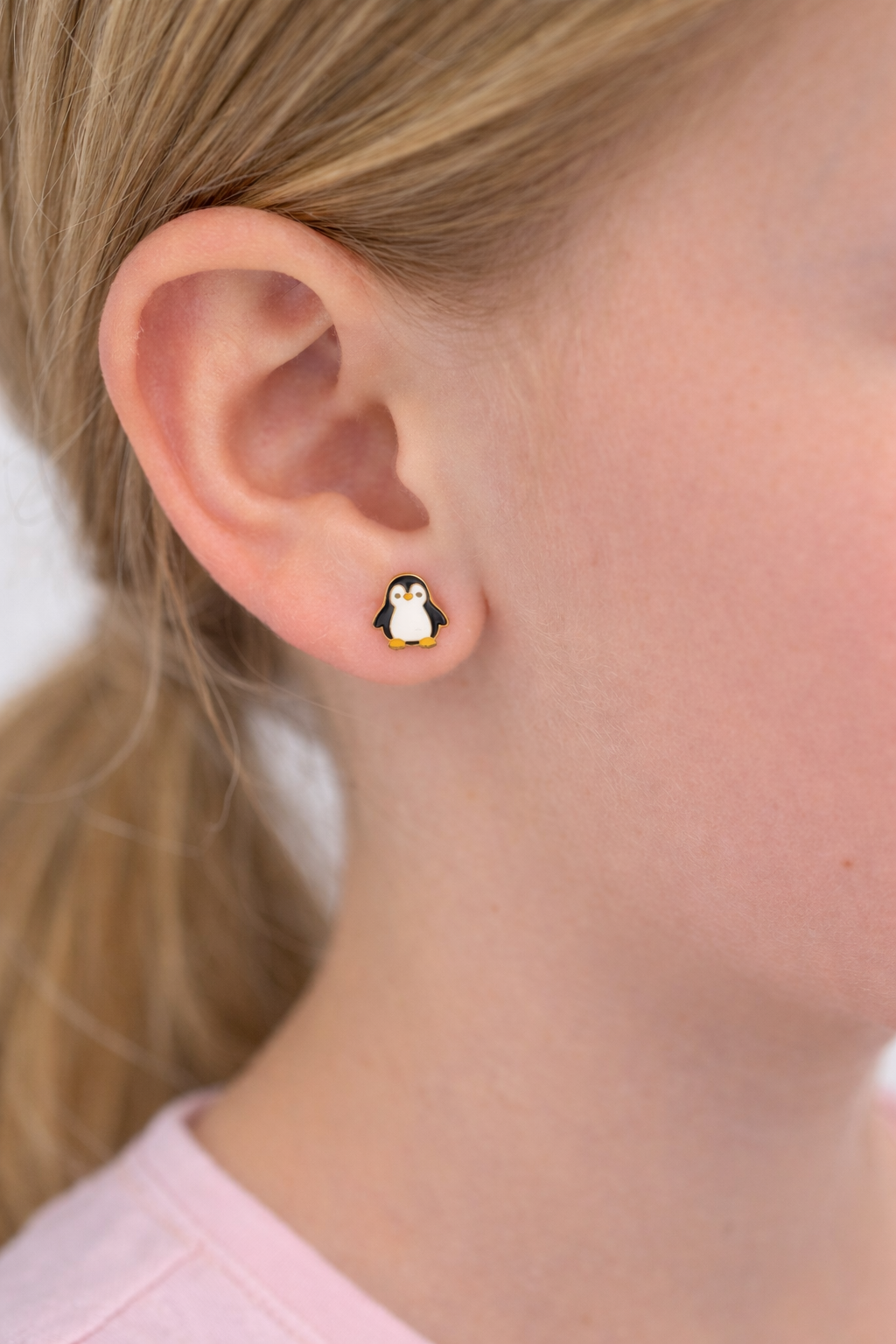 Penguin-shaped earrings worn by a person with blonde hair.