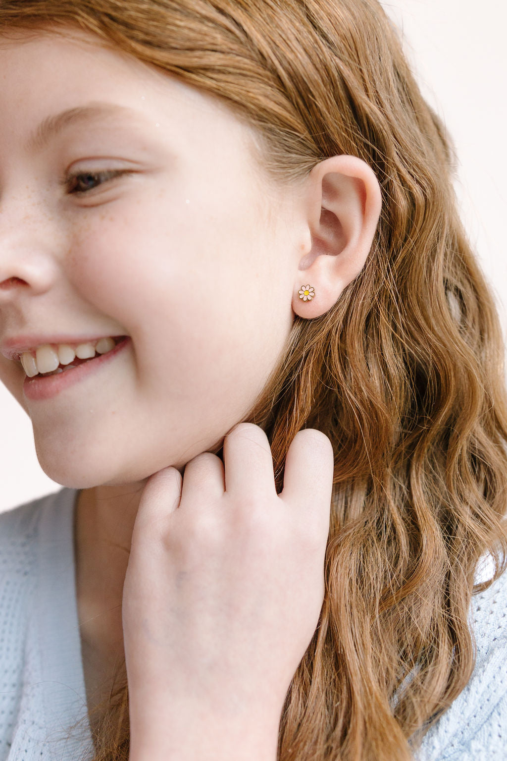 Pink daisy stud earring worn on an earlobe