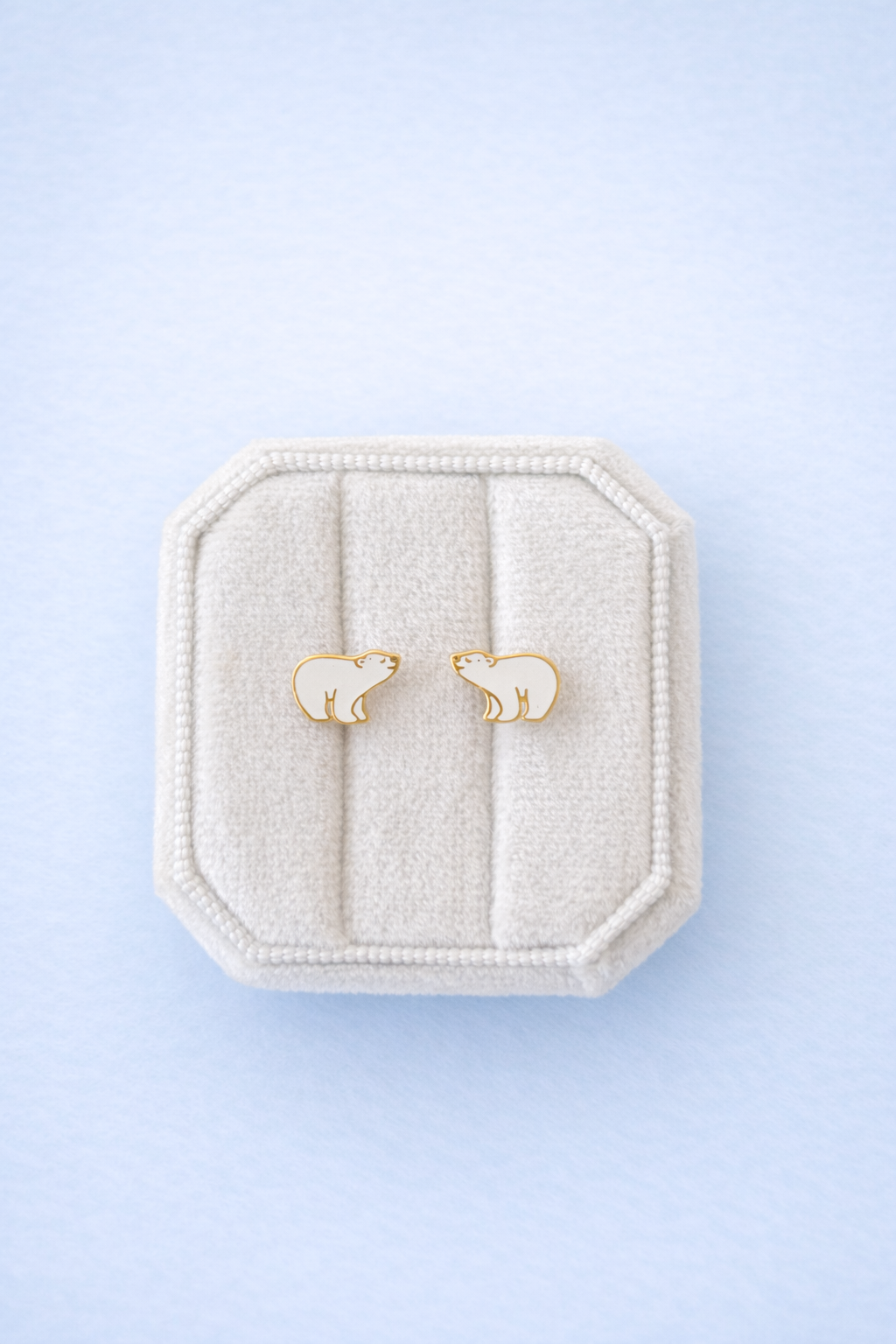 Gold bear-shaped earrings in a white jewelry box on a light blue background