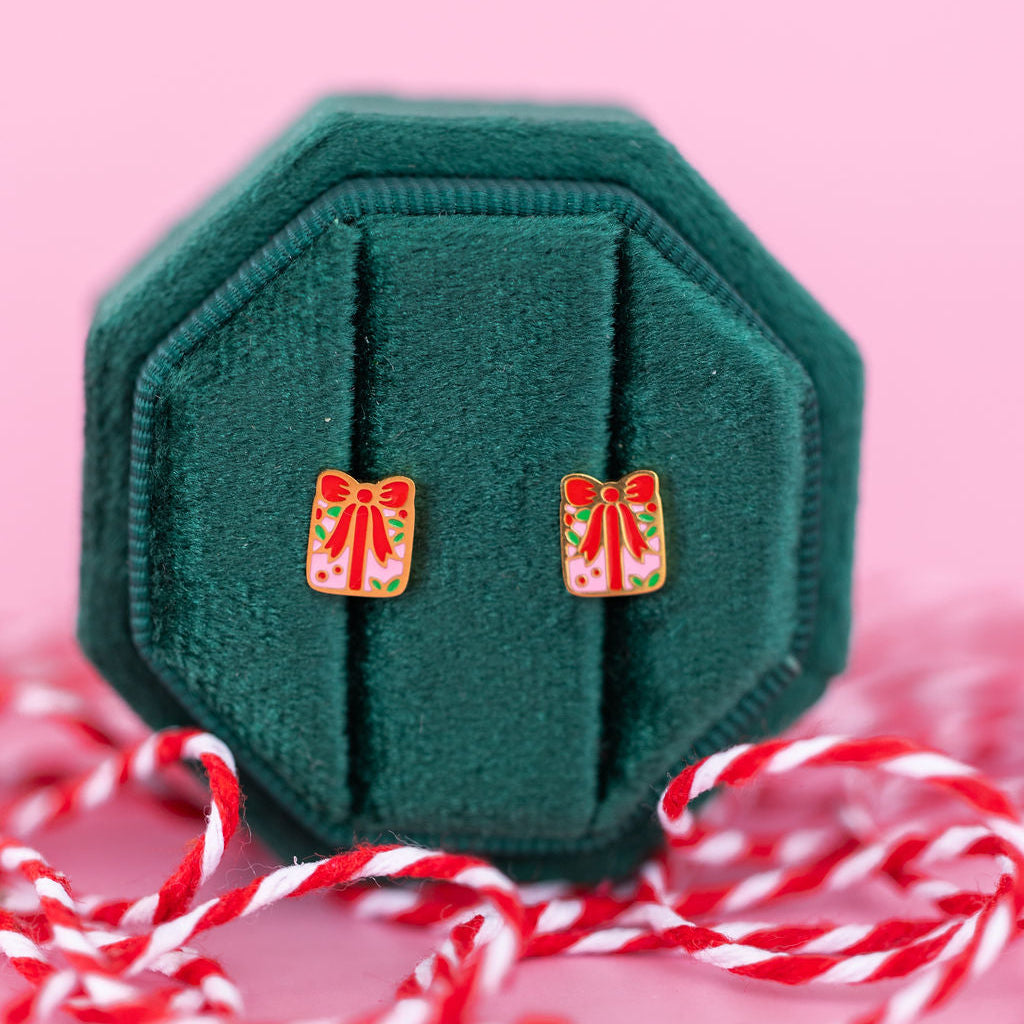 Present shaped studs in a green jewelry box sitting on candy cane colored string against a light pink background