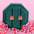 Present shaped studs in a green jewelry box sitting on candy cane colored string against a light pink background