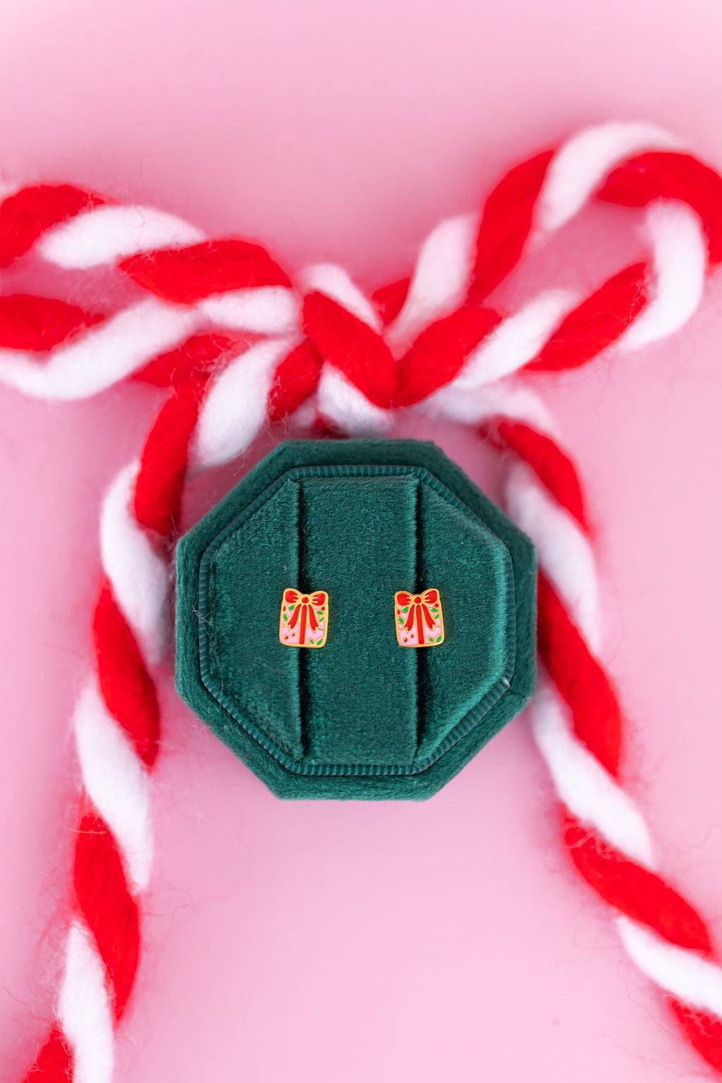 Present shaped studs in a green jewelry box sitting on candy cane colored bow against a light pink background