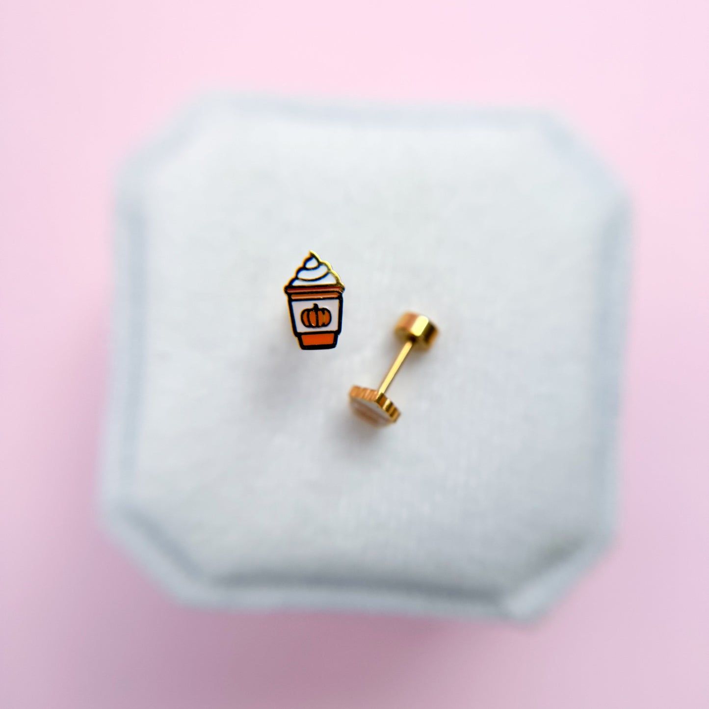 Pumpkin Spice Latte shaped earrings on a hexagonal white stand with a pink background