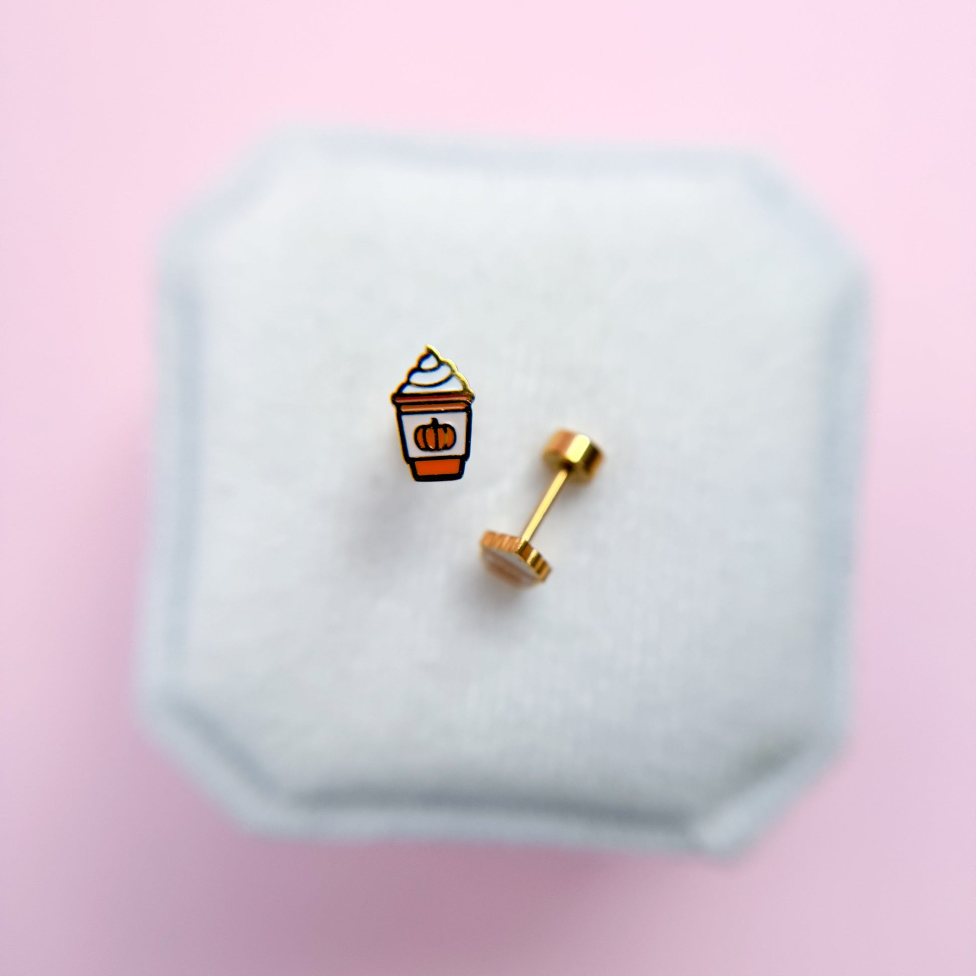 Pumpkin Spice Latte shaped earrings on a hexagonal white stand with a pink background