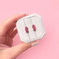 Hand holding a small white box with pink seahorse earrings against a pink background