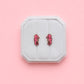 Pink seahorse earrings on a white jewelry box against a pink background