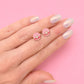 Hand holding two pink seashell-shaped earrings with pearl detail against a pink background