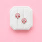 Pair of shell-shaped earrings with pearls on a white jewelry box against a pink background