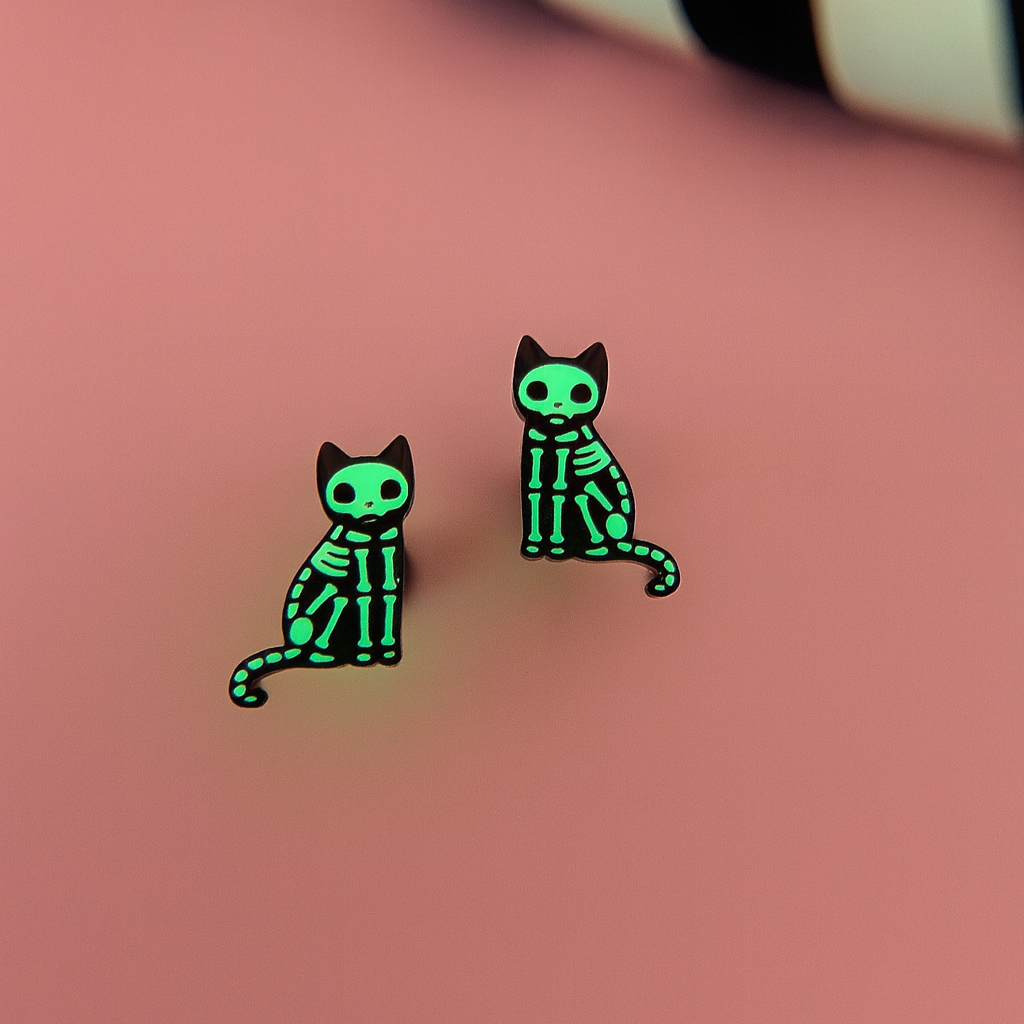 Glow in the dark green skeleton cat earrings on a pink background