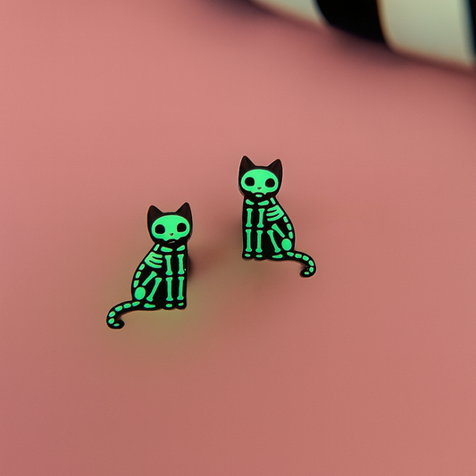 Glow in the dark green skeleton cat earrings on a pink background