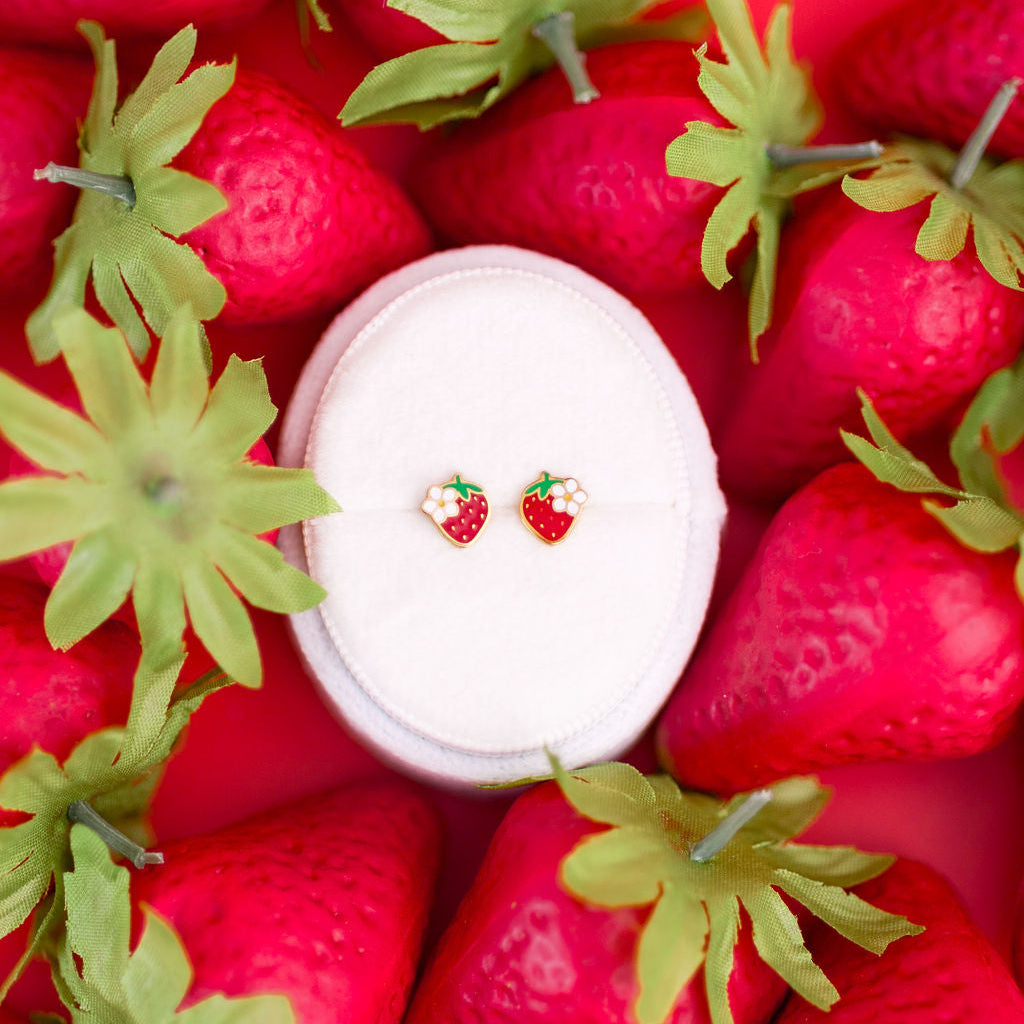 Strawberry blossom studs on a white jewelry box on a bed of strawberries