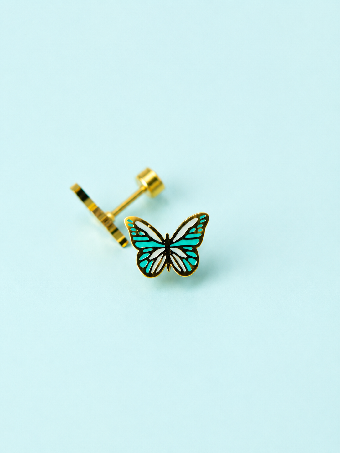 Pair of teal colored enamel butterfly stud earrings on a light blue background