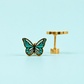 Pair of teal colored enamel butterfly stud earrings on a light blue background