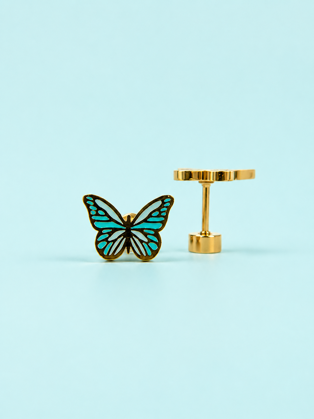 Pair of teal colored enamel butterfly stud earrings on a light blue background