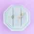 Two gold earrings in a light blue hexagonal earring holder on a purple background