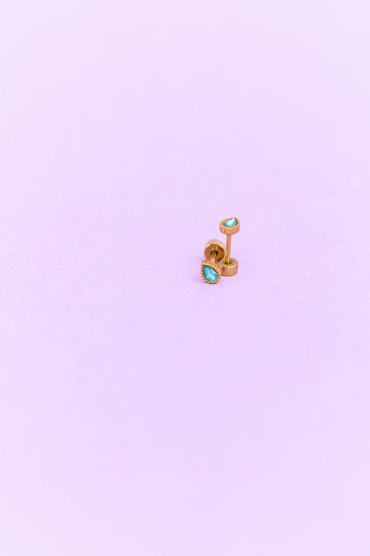 Gold earring with turquoise gemstones on a light purple background