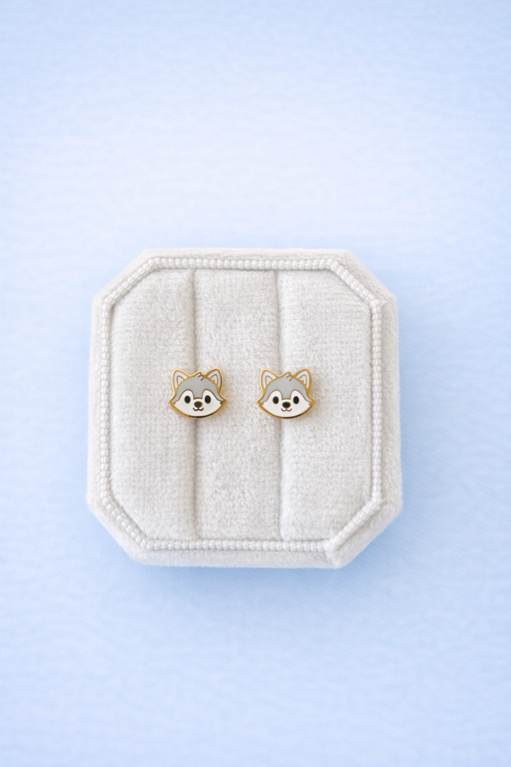 Wolf face studs in a white jewelry box on a light blue background