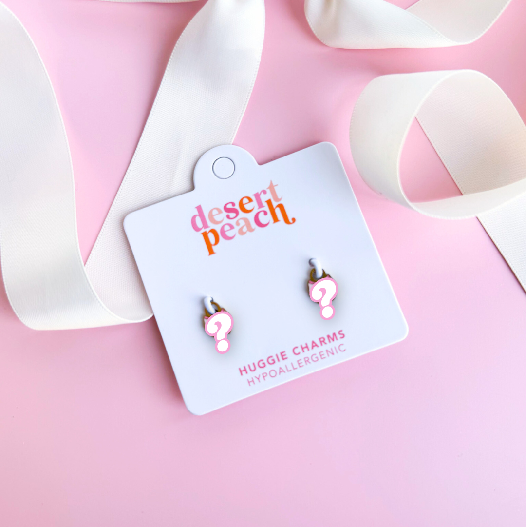 Pink earrings on a 'desert peach' branded card with a white ribbon on a pink background